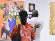 A couple at the Affordable Art Fair NYC, taking a photo of a bright, contemporary still life floral painting. 