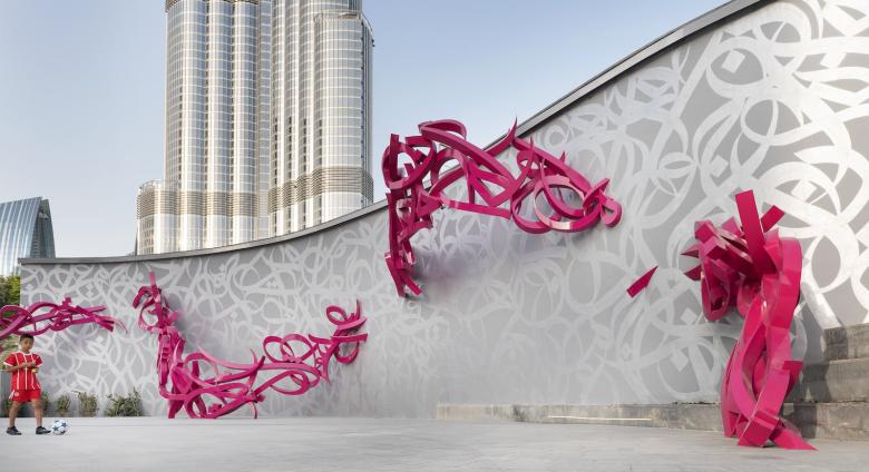 View of sculptural installation "declaration" featuring red and silver text along a scrolling wall. 