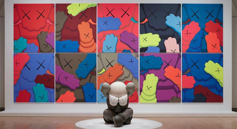 Installation view, KAWS: WHAT PARTY, Brooklyn Museum, February 26, 2021 - September 5, 2021. Features sculpture in front of a series of several flat images of 