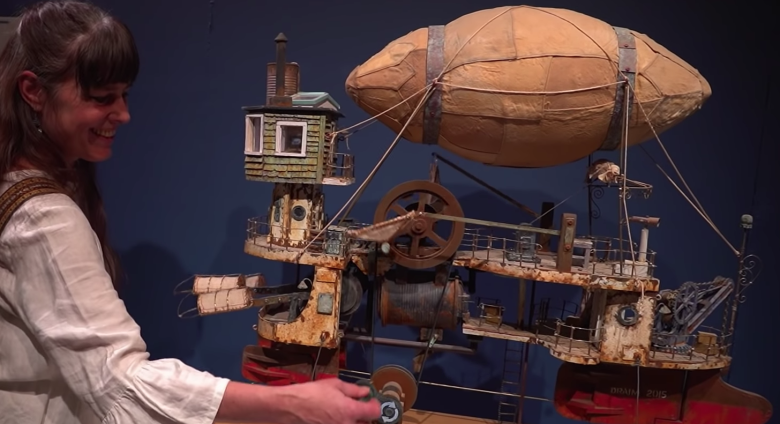 Woman turns handle of steampunk blimp ship sculpture