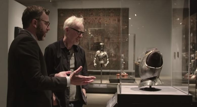 Adam Savage and Met Curator look at child's breastplate in glass case