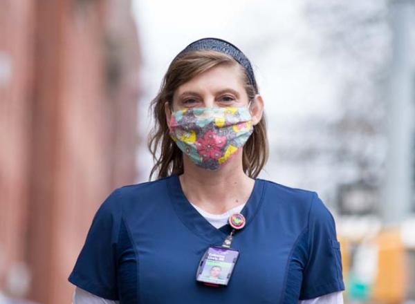 Catherine “Cat” Carnes, a registered nurse, stands on the street wearing a mask and scrubs