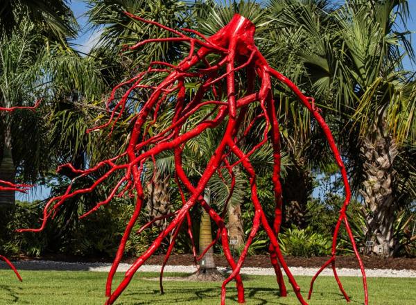 large red metal sculpture of roots in a garden